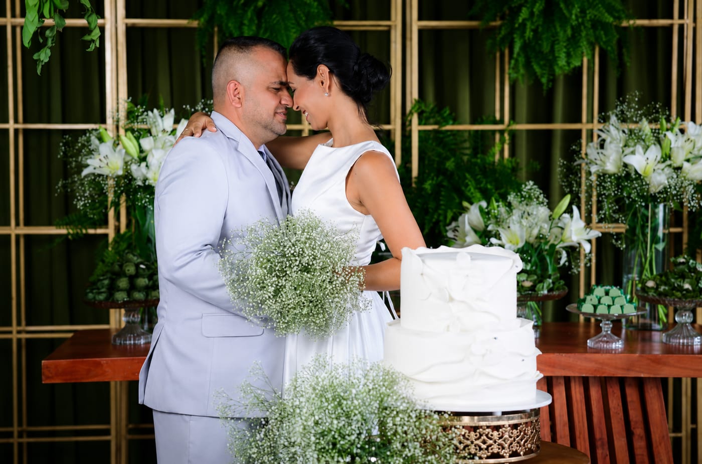 Noivos cortando o bolo de casamento na decoração com folhagens
